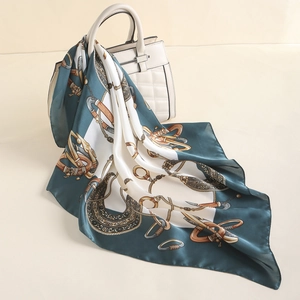 Elegant silk-like square scarf with gold equestrian patterns draped on a white handbag