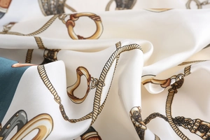 Detailed close-up of ivory silk scarf fabric with vintage horse bit and chain patterns