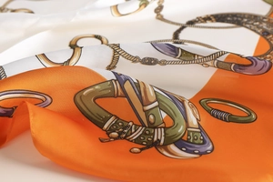 Detail of luxury silk scarf showing orange equestrian patterns and golden chain texture