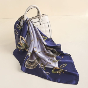 Detail of silk-like square scarf with horse bridle print draped on white handbag