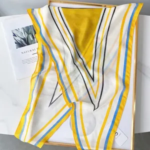 Minimalist geometric striped silk scarf in yellow and blue, styled on a wooden tray