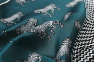 Detailed view of teal silk scarf featuring artistic horse patterns and geometric borders