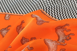 Detail of luxury orange silk scarf featuring vintage horse prints and smooth texture