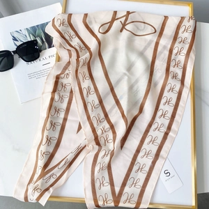 Flat lay of cream silk scarf with brown H-print and stripes on marble background