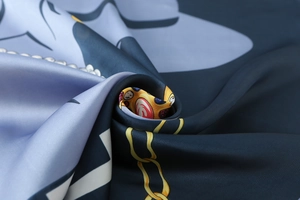 Macro view of luxurious silk-like scarf featuring golden chains and navy blue paisley patterns