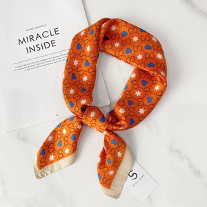 Macro view of smooth orange silk scarf with gold border and artistic patterns