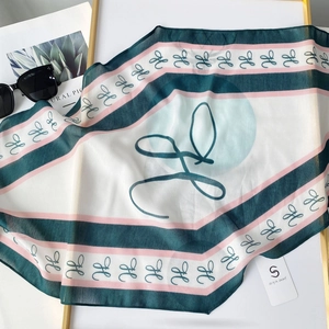 Detail of thin diamond-shaped silk scarf with green and pink letter H pattern