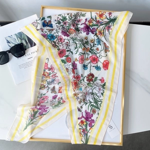 Détail d'un foulard en soie aux imprimés floraux colorés et bordures jaunes sur marbre