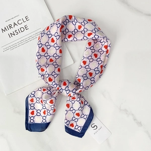 Detailed close-up of a silk scarf with blue S-pattern and red hearts on marble surface