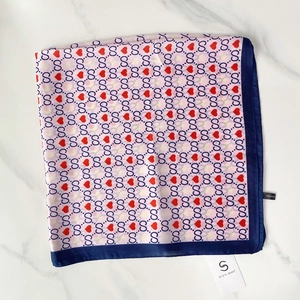 Detail of silk-like square scarf with gold trim, heart patterns, and polyester material tag