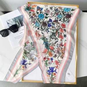 Détail d'un foulard en soie à fleurs et papillons sur plateau doré et marbre blanc