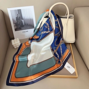 Detail view of a luxury silk scarf with chain print draped over a white leather handbag