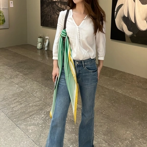 Detail shot of a white V-neck blouse paired with a striped navy silk scarf on the shoulder