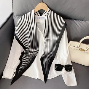 Detail of white satin shirt paired with a chic navy striped silk scarf on a wooden hanger
