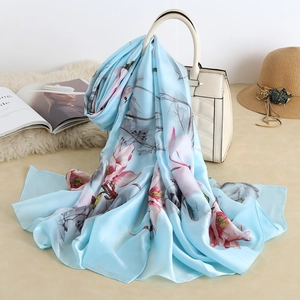 Detailed view of light blue silk-like scarf with floral prints draped on a white handbag
