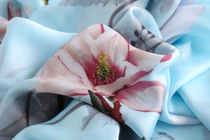 Detail of elegant magnolia print on soft light blue silk scarf fabric with smooth texture
