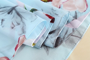 Close-up of lightweight light blue silk scarf with elegant pink floral prints and fine stitching