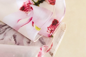 Detailed macro view of magnolia floral print on elegant pink silk scarf with rolled edges