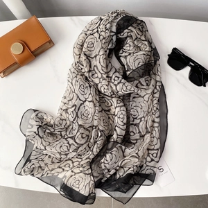 Detail of thin camellia silk scarf with black floral print on white marble surface