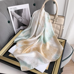 Detail of silk-feel scarf with artistic print draped over a stylish cream handbag