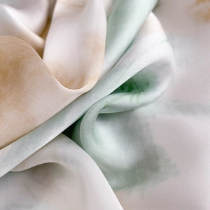 Close-up of lightweight silk-feel fabric with green tie-dye pattern and twill texture