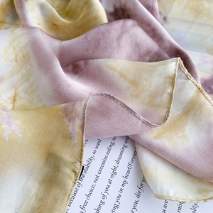 Close-up of tie-dye silk scarf showing yellow and purple textures and machine-rolled edges