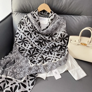 Elegant geometric and floral print scarf shawl displayed on a wooden hanger over leather
