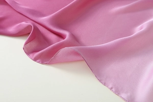 Detailed close-up of smooth peach pink satin silk scarf fabric with premium hemmed edges