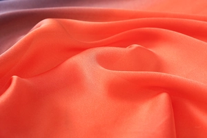 Detailed close-up of vibrant coral orange silk scarf fabric with elegant soft folds