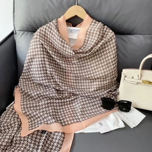 Close-up of brown houndstooth pattern scarf with peach pink borders on wooden hanger