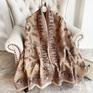Dettaglio della sciarpa beige motivo paisley simil cashmere con frange sulla sedia