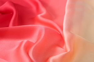 Macro shot of gradient silk fabric transition from coral red to light orange pink