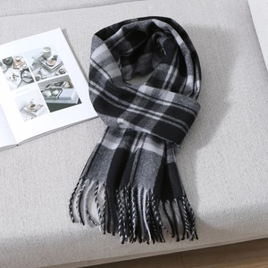 Detailed view of black and white plaid scarf with fringe tassels on a soft sofa