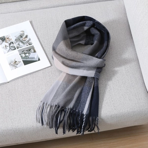 Close-up of classic blue and beige plaid scarf with soft fringe details on a grey sofa