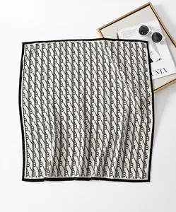 Close-up of geometric pattern square silk scarf with black borders shown on a tray