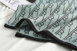 Close-up of light blue silk scarf with black monogram B pattern and fine twill texture