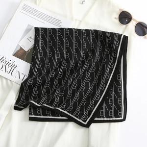 Detail of soft wool-feel scarf featuring black and white monogram pattern and brand tag