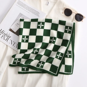 Flat lay of green and white checkerboard silk scarf with flower patterns and sunglasses