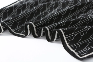 Close-up of black knit silk scarf featuring white letter B patterns and striped border