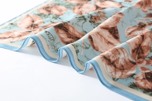 Close-up of sky blue twill silk scarf featuring autumn leaf prints and fine stitching