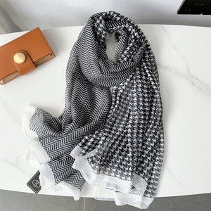 Detail of houndstooth and herringbone pattern scarf on marble surface with gold tag
