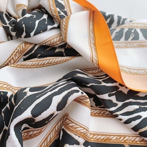 Détail de foulard en satin avec motif zèbre, chaînes dorées et bordure orange vif