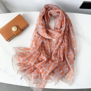 Close-up of lightweight orange and beige geometric scarf on white marble background