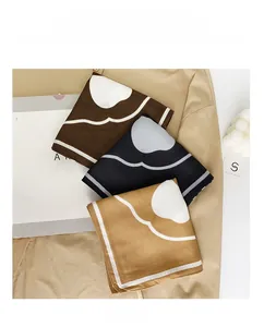 Dettaglio di tre foulard effetto seta in marrone, nero e giallo con motivi a nuvola