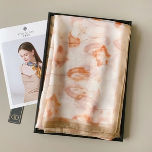 Detail view of floral print silk scarf with smooth satin texture and elegant orange patterns