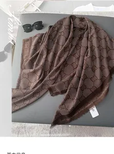 Detail of dark brown scarf with monogram pattern and fringe, showing soft texture