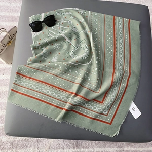 Detail of sage green silk scarf with vintage key patterns and tassel edge on a leather surface