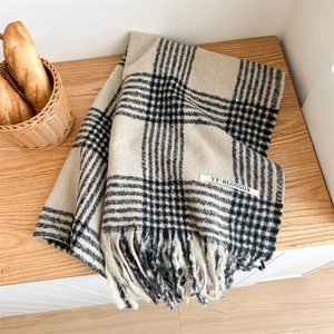 Detail of beige plaid scarf with soft fringe edges and branded label on wooden surface