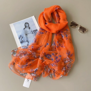 Detailed flat lay of orange floral chiffon scarf with sunglasses and brand tag