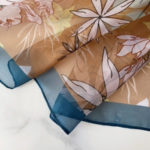 Detail of floral print scarf with blue edges on white marble showing soft sheer texture